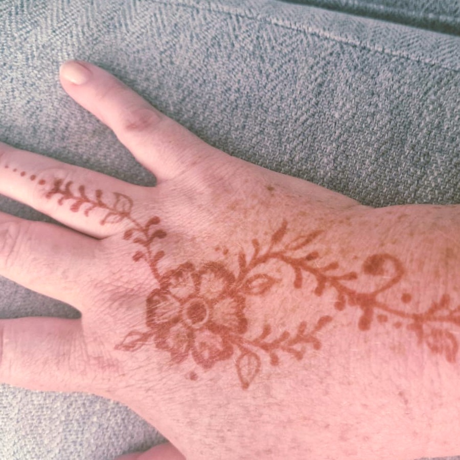 Flower and vine henna design in warm next-day colour on the back of the hand