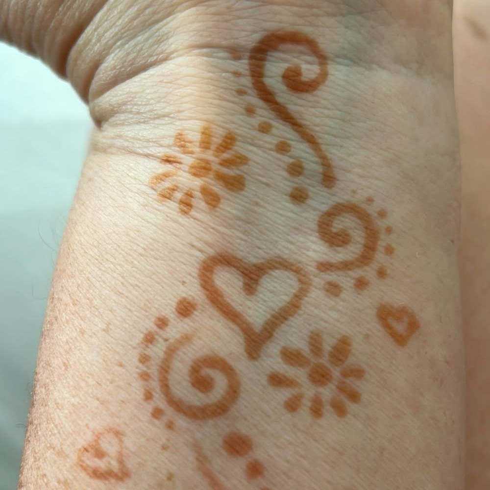 Heart and floral swirl henna design in warm next-day colour on the wrist